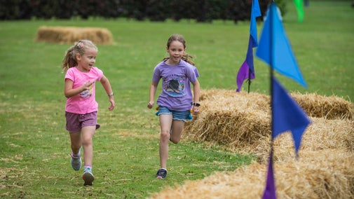 Two young girls racing along a course, marked out by straw bales, towards a string of colourful bunting